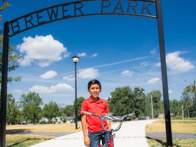 Photo of a kid sitting on a bike under a sign for Brewer Park 